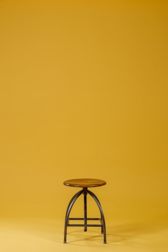 round brown wooden top and black base chair on yellow background