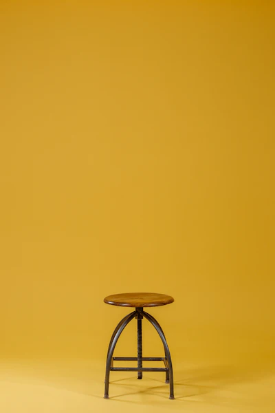 A wooden stool against a yellow wall