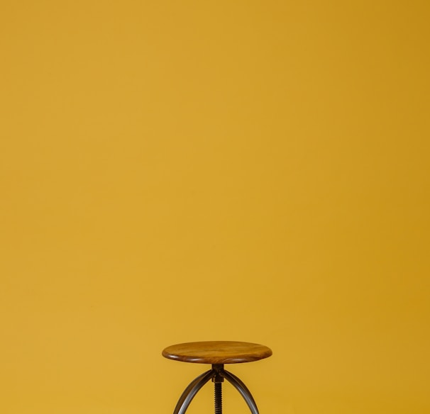 round brown wooden top and black base chair on yellow background