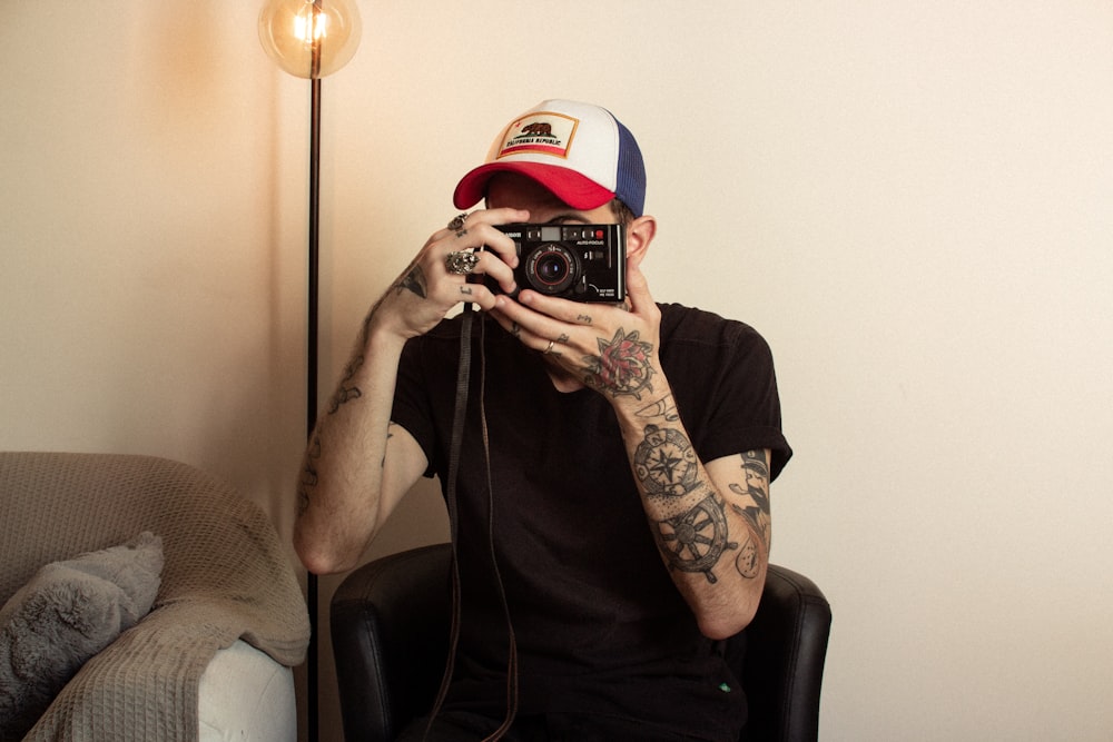 man holding camera while sitting on tub chair