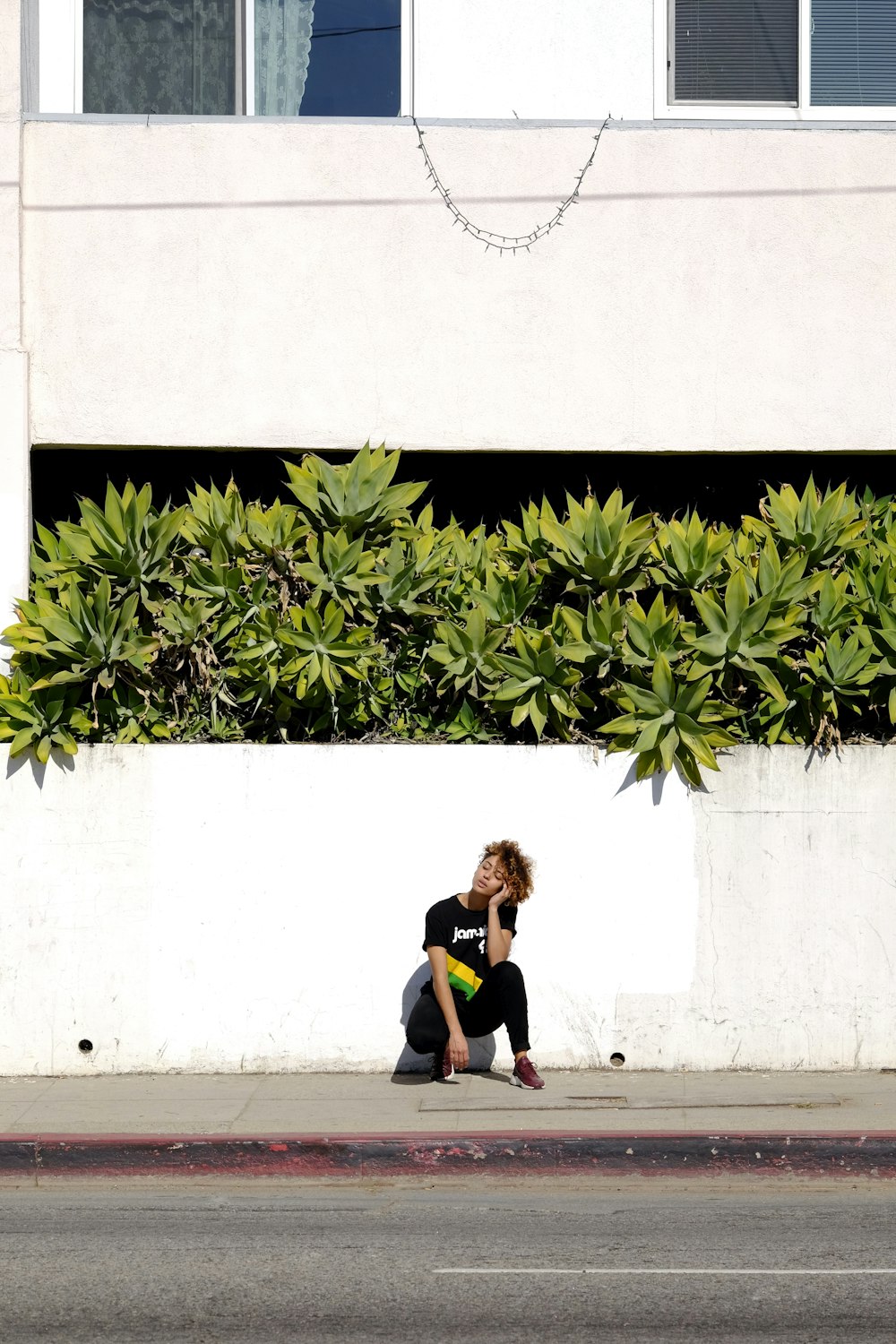 woman sitting near wall with plant