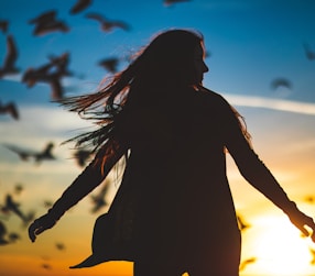 silhouette photography of woman spreading her hands in front of flight of birds