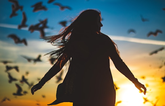 silhouette photography of woman spreading her hands in front of flight of birds
