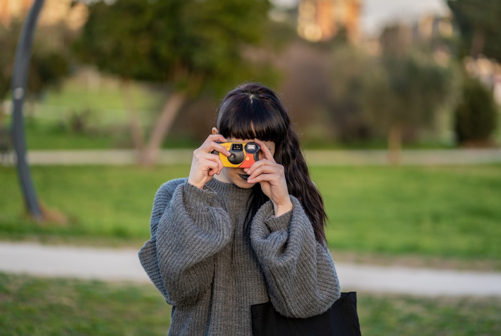 Donna che indossa un maglione lavorato a maglia grigio che tiene una fotocamera gialla point-and-shoot