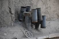 Close-up of rusted pipes intertwined with wires, dripping with dark liquid against a concrete wall.