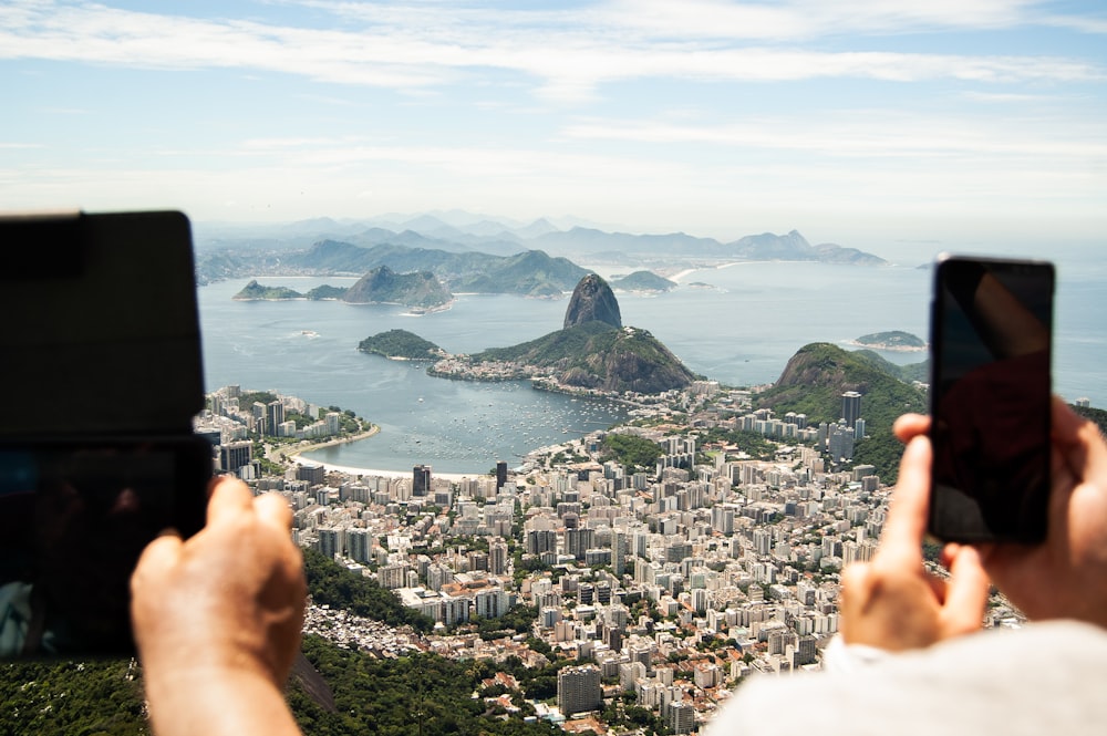 two person holding tablet computer and smartphone in elevated place with the view of city during daytime