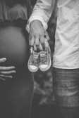 grayscale photo of man and woman holding baby's low-top shoes