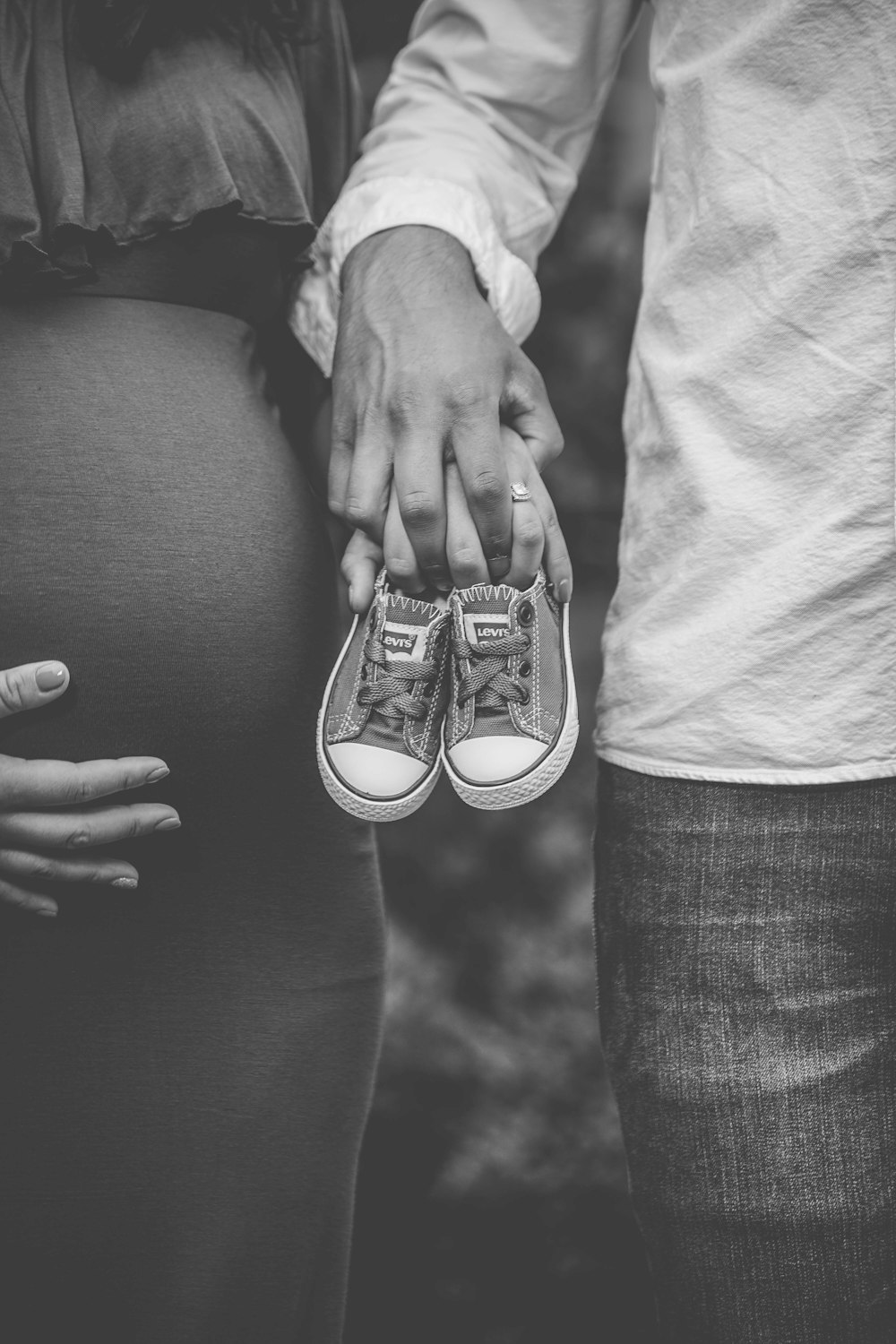 grayscale photo of man and woman holding baby's low-top shoes