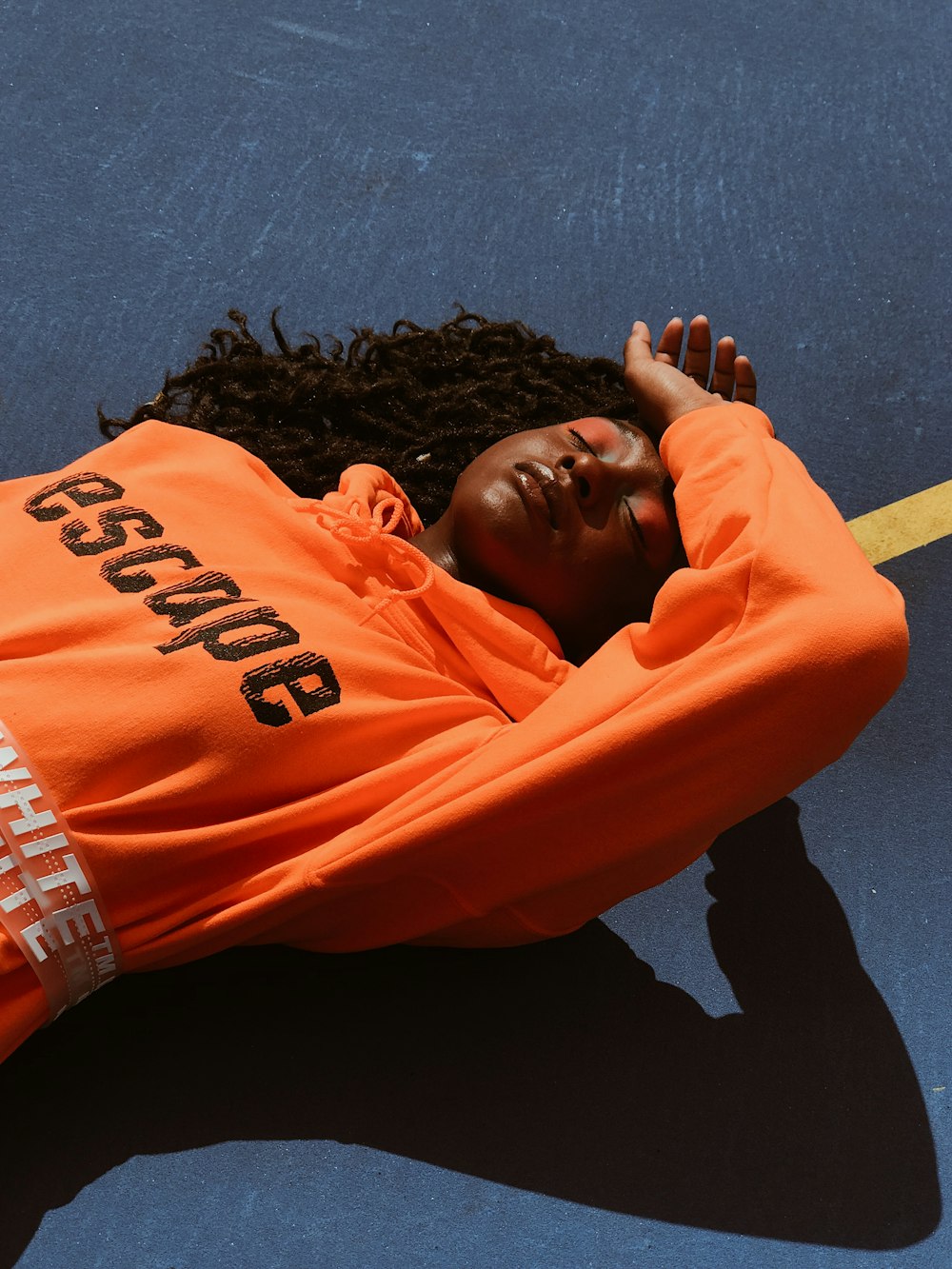 woman wearing orange pullover hoodie lying on road