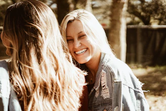 A group of diverse women laughing together during an outdoor nature hike in a sunny forest.