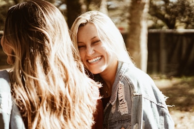 Two women laughing together on a sunlit mountain trail, backpacks on and ready for adventure.