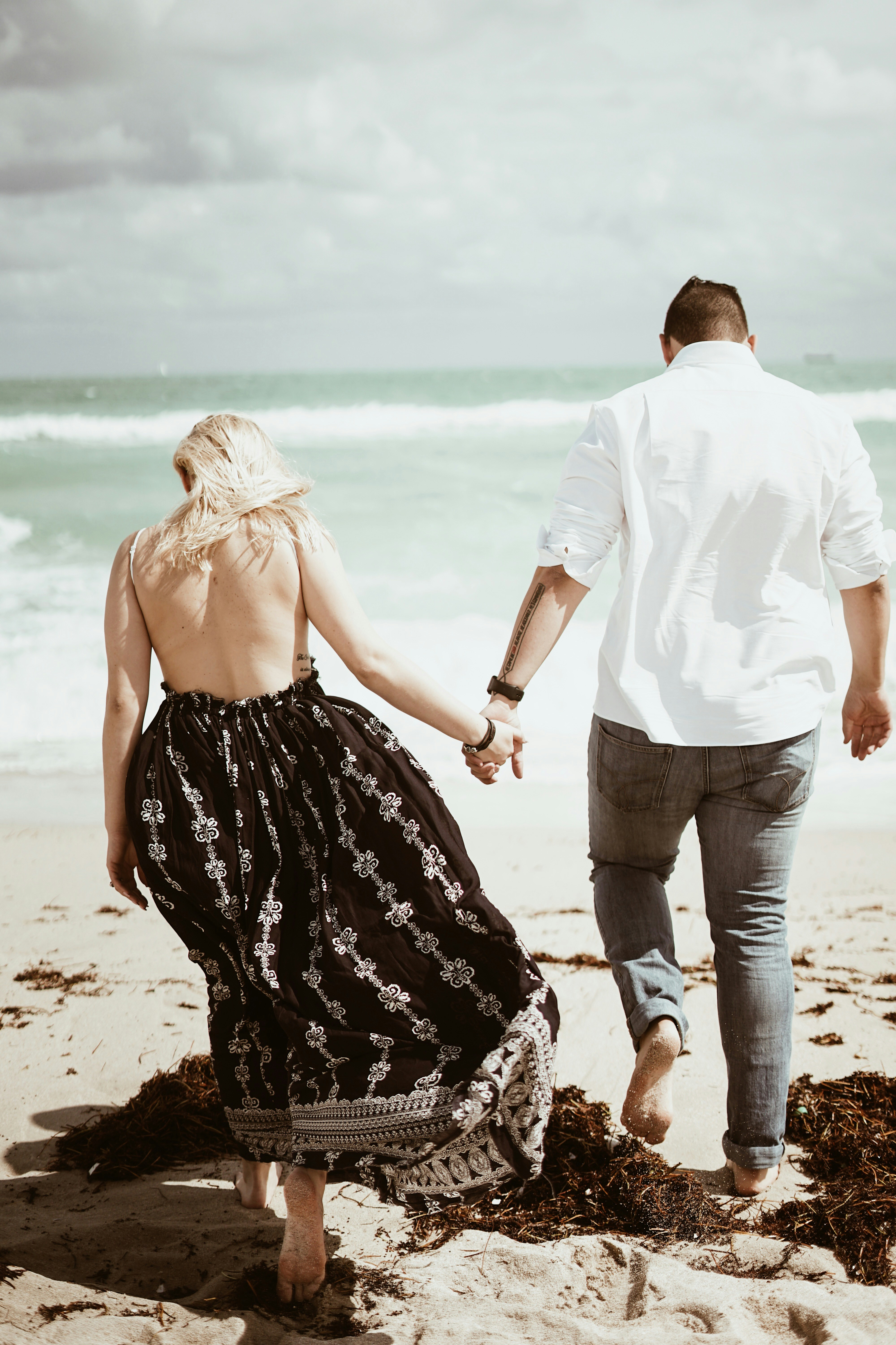 couple walking on sand near beach during daytime