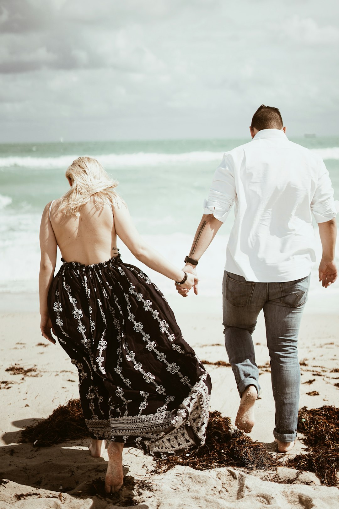 couple walking on sand near beach during daytime
