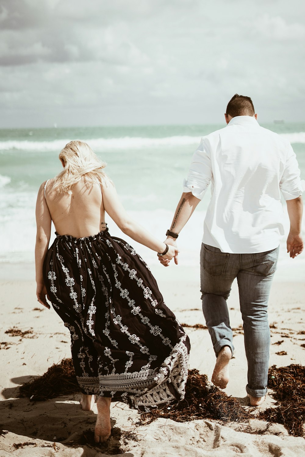 couple walking on sand near beach during daytime