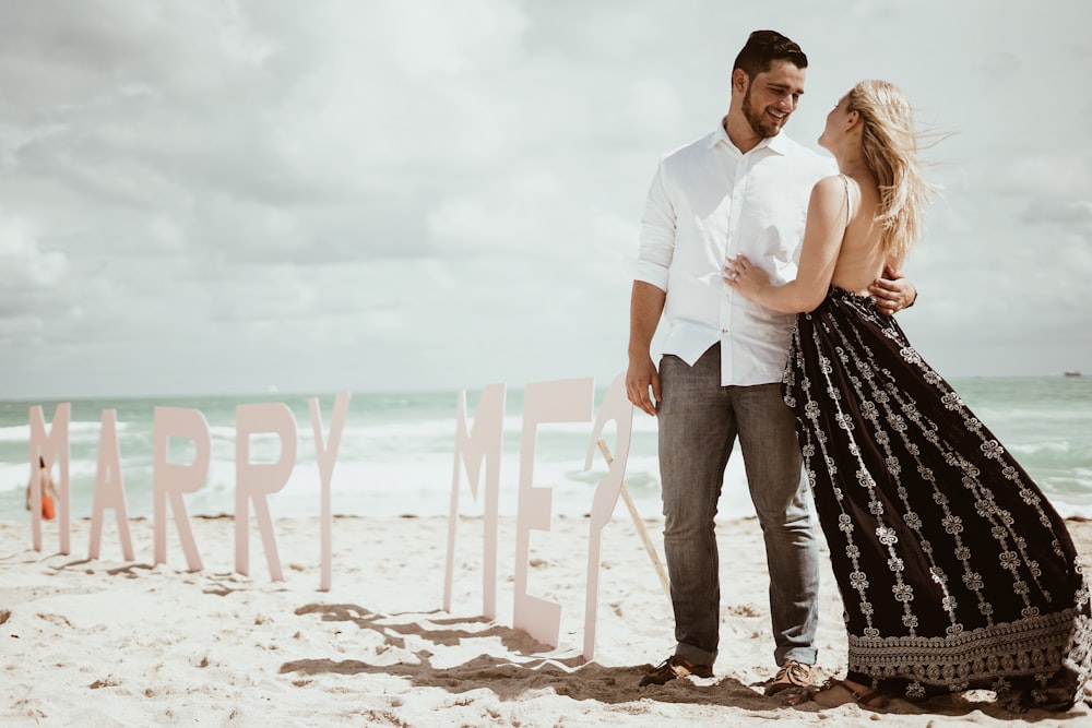 couple standing on marry me freestanding on beach