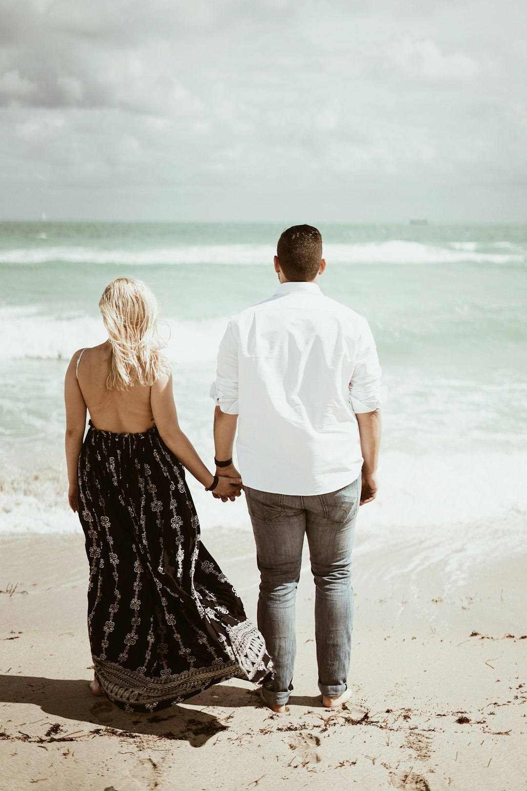 man and woman holding each other's hands and walking by the seashore during daytime