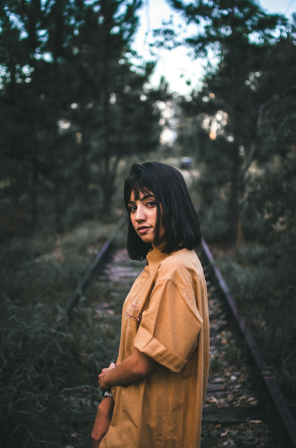 woman standing on train railway surrounded by trees