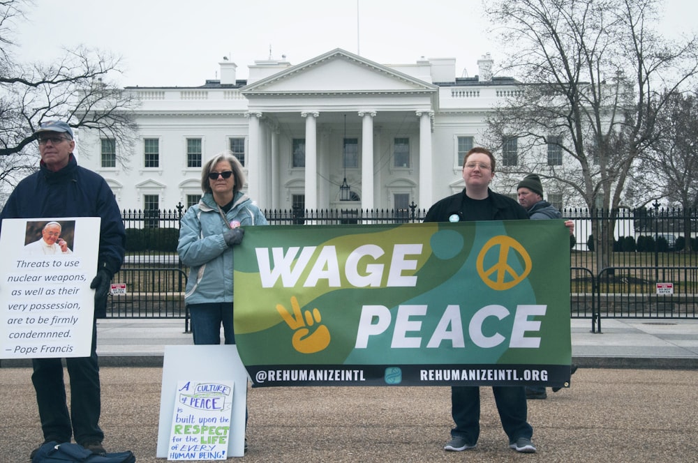 people holding Wage Peace signage in front of white concrete building during daytime