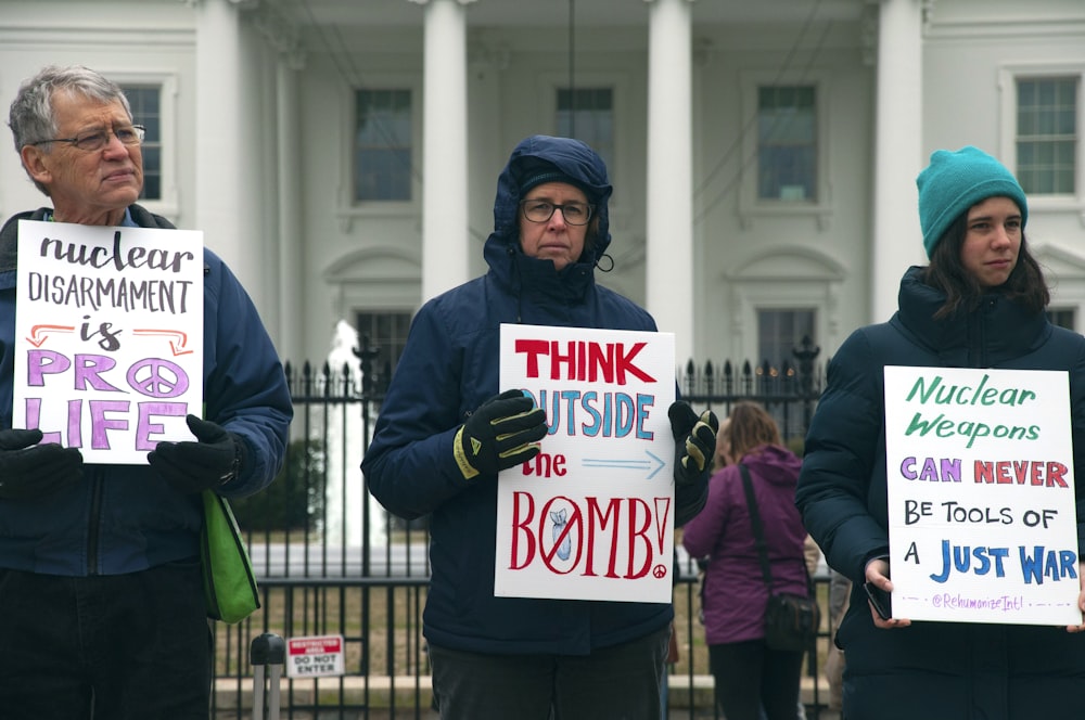 tres hombres y mujeres sosteniendo carteles frente a la Casa Blanca, Washington D.C. durante el día