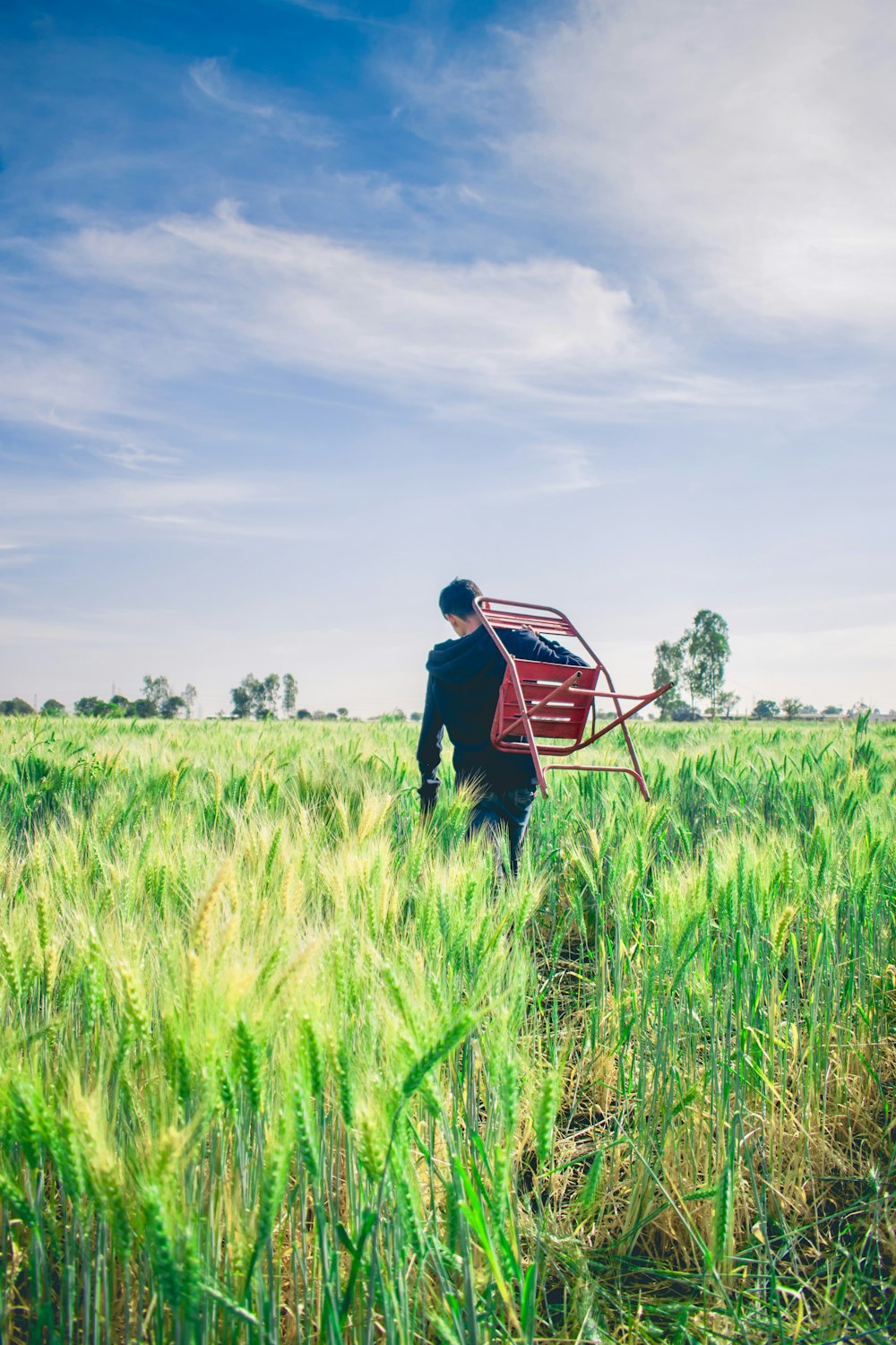 man in black sweater carrying chair in middle of field