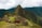 A breathtaking view of Machu Picchu with its ancient ruins set against a backdrop of lush green mountains. A llama grazes in the foreground, adding to the scene's authenticity and charm. The sky is overcast with clouds hovering over the peaks.