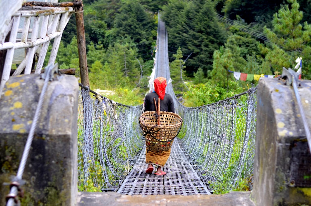 person walking at bridge while carrying brown basket