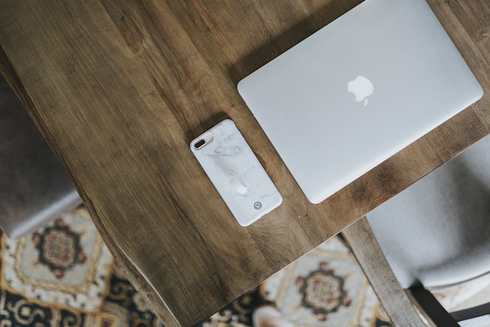 MacBook silver and silver iPhone case on top of brown wooden table