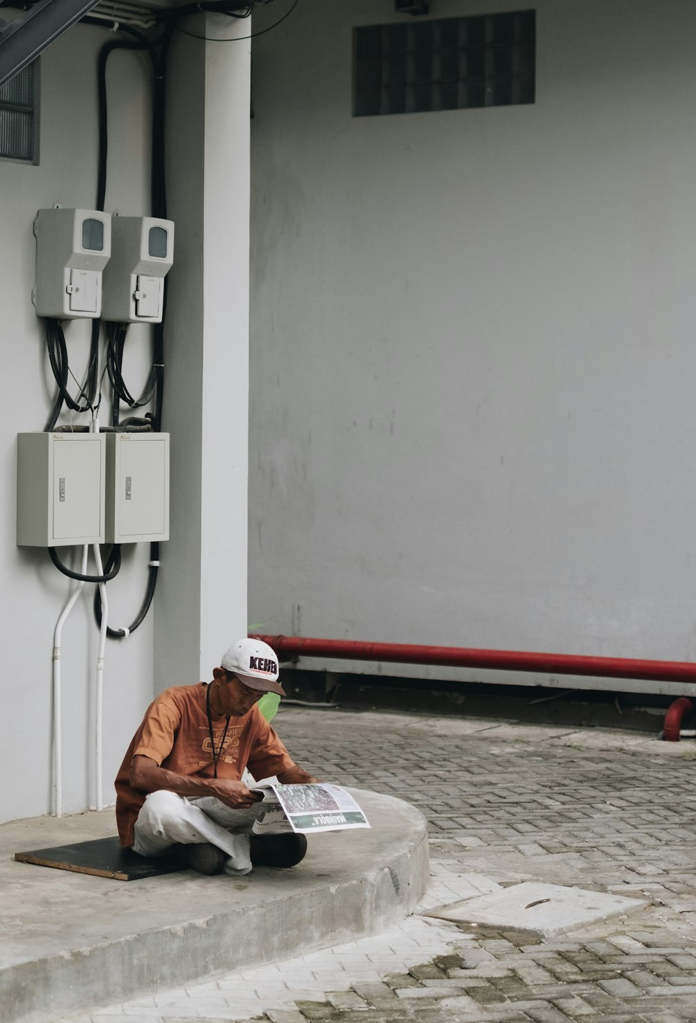 man wearing orange shirt sitting on concrete pavement during daytime