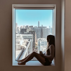 woman sitting in window sill looking outside