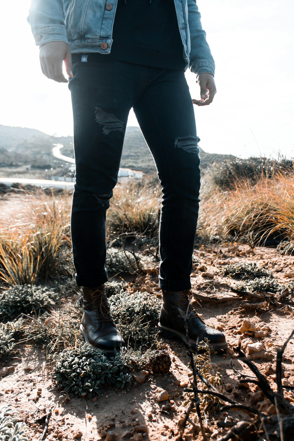 Persona con pantalones negros y botas marrones de pie en un campo de hierba marrón durante el día