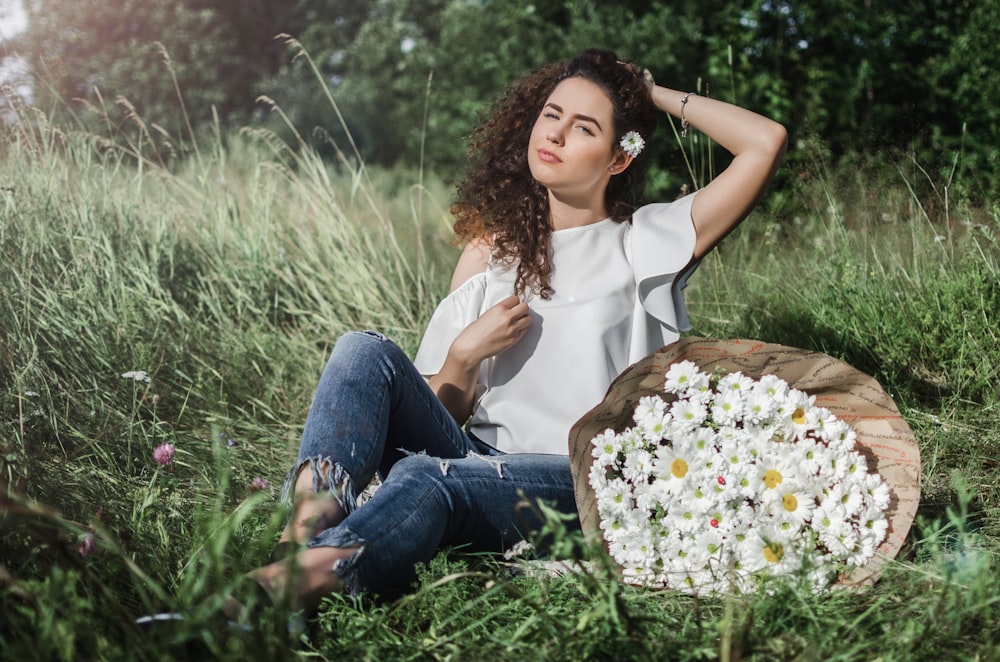 Mujer sentada en el campo de hierba verde con la flor durante el día