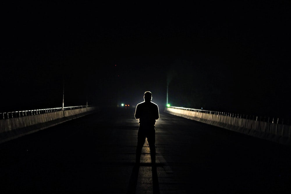 silhouette of man standing in the middle of asphalt road