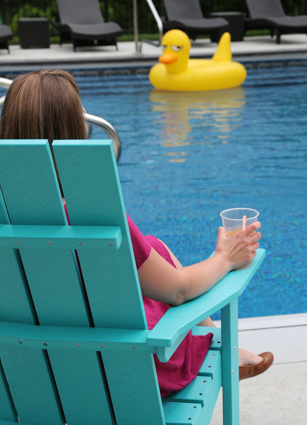 woman sitting on blue wooden armchair facing on swimming pool during daytime