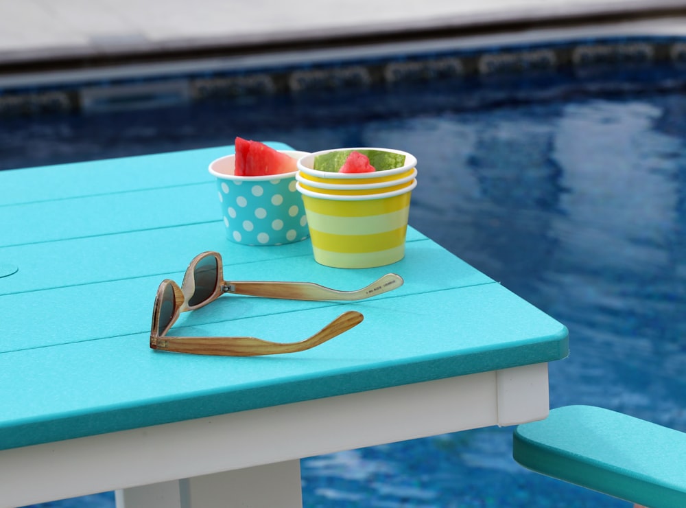 sunglasses beside cups on table near pool