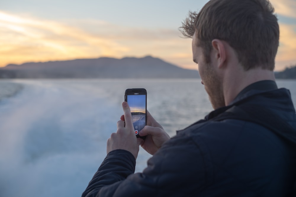 man taking photo of snow covered lake during sunrise