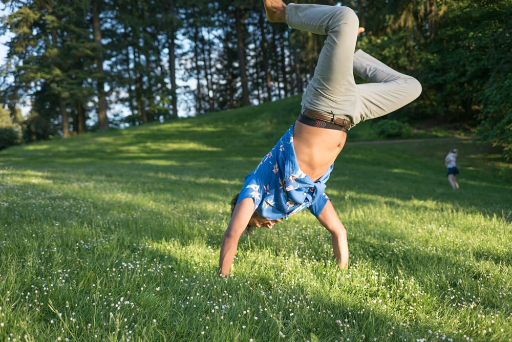 man in blue shirt and jeans standing upside down in grass field