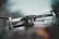 A sleek black drone captured in mid-air, with detailed focus on its camera and hardware. The background is a soft blur, emphasizing a smooth bokeh effect and providing a sense of motion.