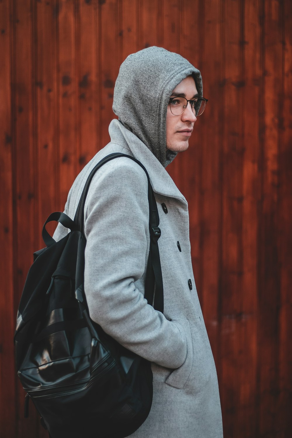 standing man wearing gray coat and carrying black backpack