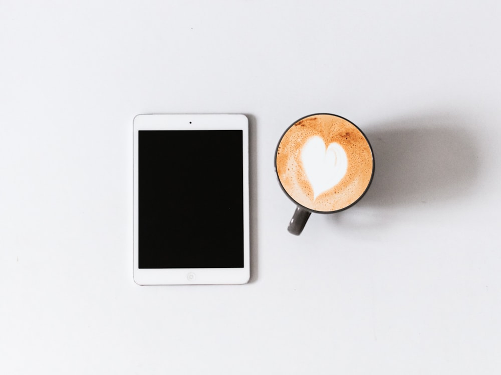 white iPad beside black ceramic mug