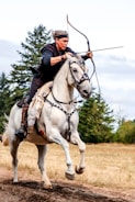 man riding white horse using composite bow