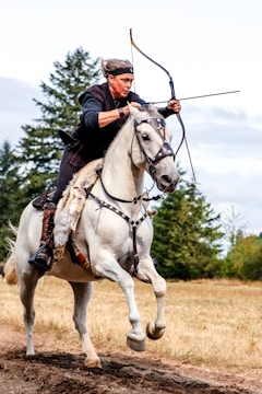 man riding white horse using composite bow