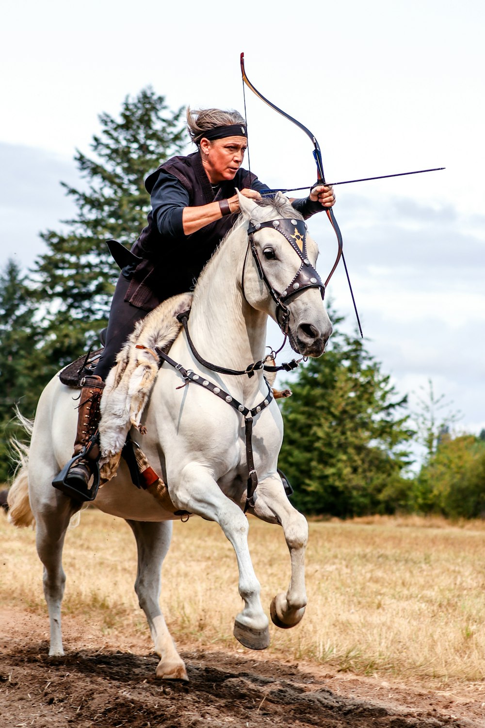 man riding white horse using composite bow