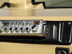 A vintage RadioShack TRC-447 CB radio installed in a vehicle dashboard. The device features various knobs and buttons for controls like volume, squelch, and gain. The dashboard is beige and black with a textured surface and mounting screws.