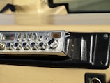 A vintage RadioShack TRC-447 CB radio installed in a vehicle dashboard. The device features various knobs and buttons for controls like volume, squelch, and gain. The dashboard is beige and black with a textured surface and mounting screws.