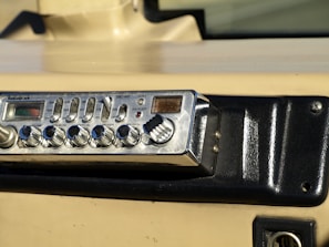 A vintage RadioShack TRC-447 CB radio installed in a vehicle dashboard. The device features various knobs and buttons for controls like volume, squelch, and gain. The dashboard is beige and black with a textured surface and mounting screws.