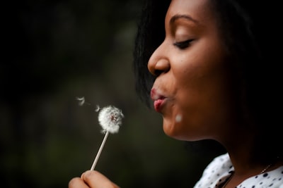 woman in white top blowing dandelion wish teams background