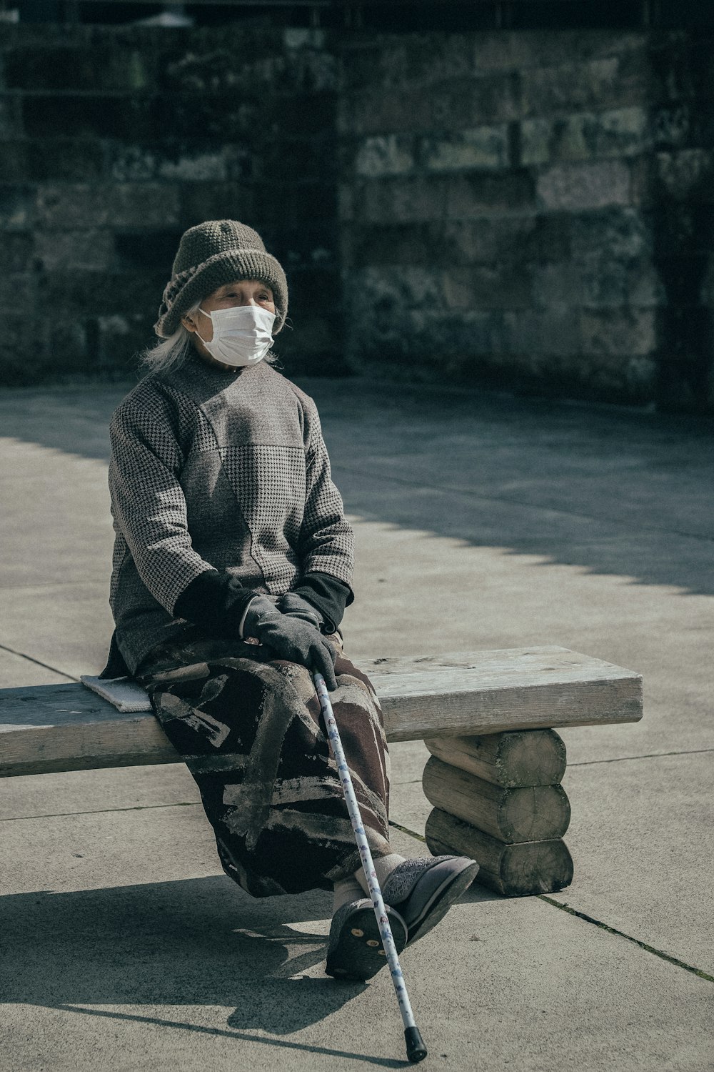 woman wearing face mask holding walking stick sitting on concrete bench