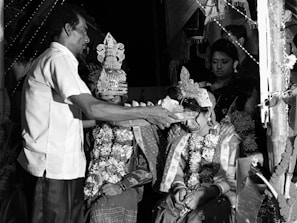A Batak couple performing a cultural ritual surrounded by deep gold and ivory ceremonial decorations.