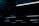 A series of linear fluorescent lights hanging from a ceiling in a dark, industrial setting. The lights cast a minimal blue glow, creating a stark contrast against the otherwise dim environment.