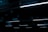 A series of linear fluorescent lights hanging from a ceiling in a dark, industrial setting. The lights cast a minimal blue glow, creating a stark contrast against the otherwise dim environment.